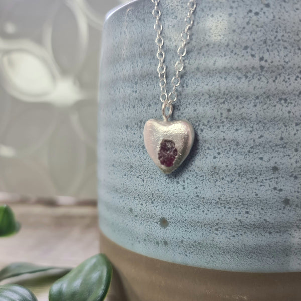 Heart-shaped pendant necklace with a gemstone on a ceramic vase
