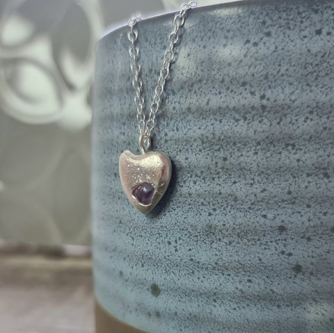 Heart-shaped pendant necklace with an amethyst stone on a textured surface