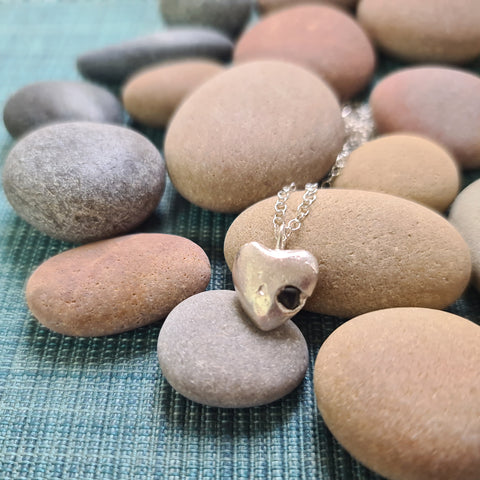 Heart-shaped pendant necklace on pebbles with a textured blue fabric background