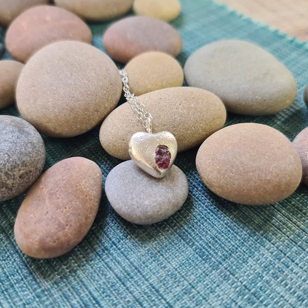 Heart-shaped pendant with a red ruby gemstone on pebbles
