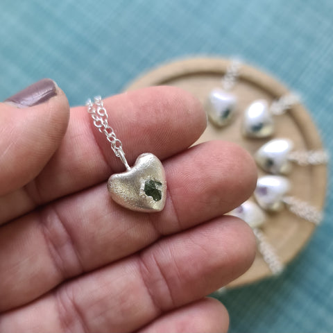 Silver heart-shaped pendant held between fingers with blurred jewelry display in the background